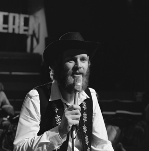 Gerard Schoonebeek met cowboyhoed en baard zingt in een microfoon in Op volle toeren, 1980