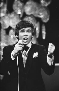 John Lamers in smoking zingt achter de microfoon op het Nationaal Songfestival van 1969